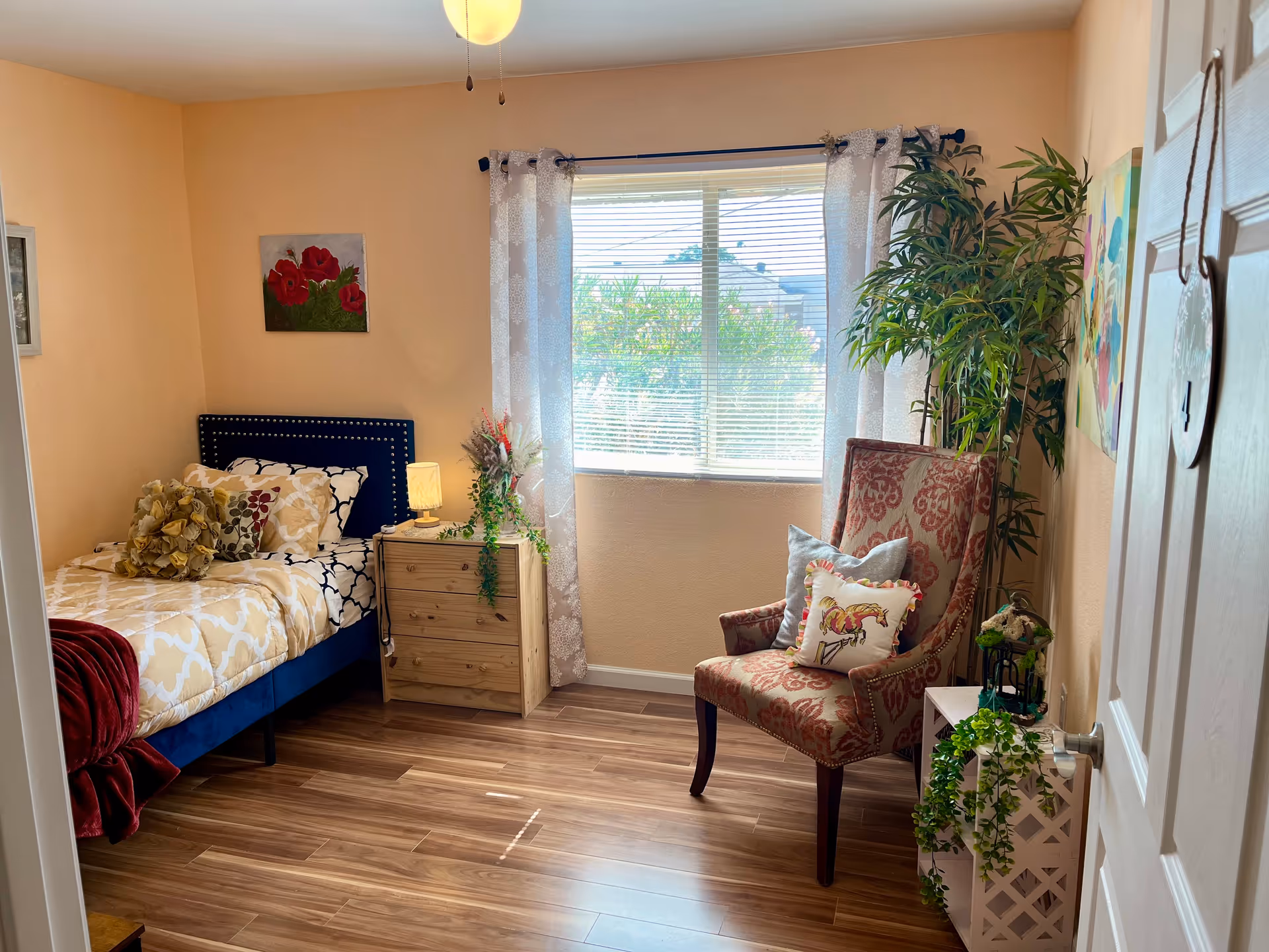 Cozy bedroom featuring a bed, nightstand, chair, window, and plants.