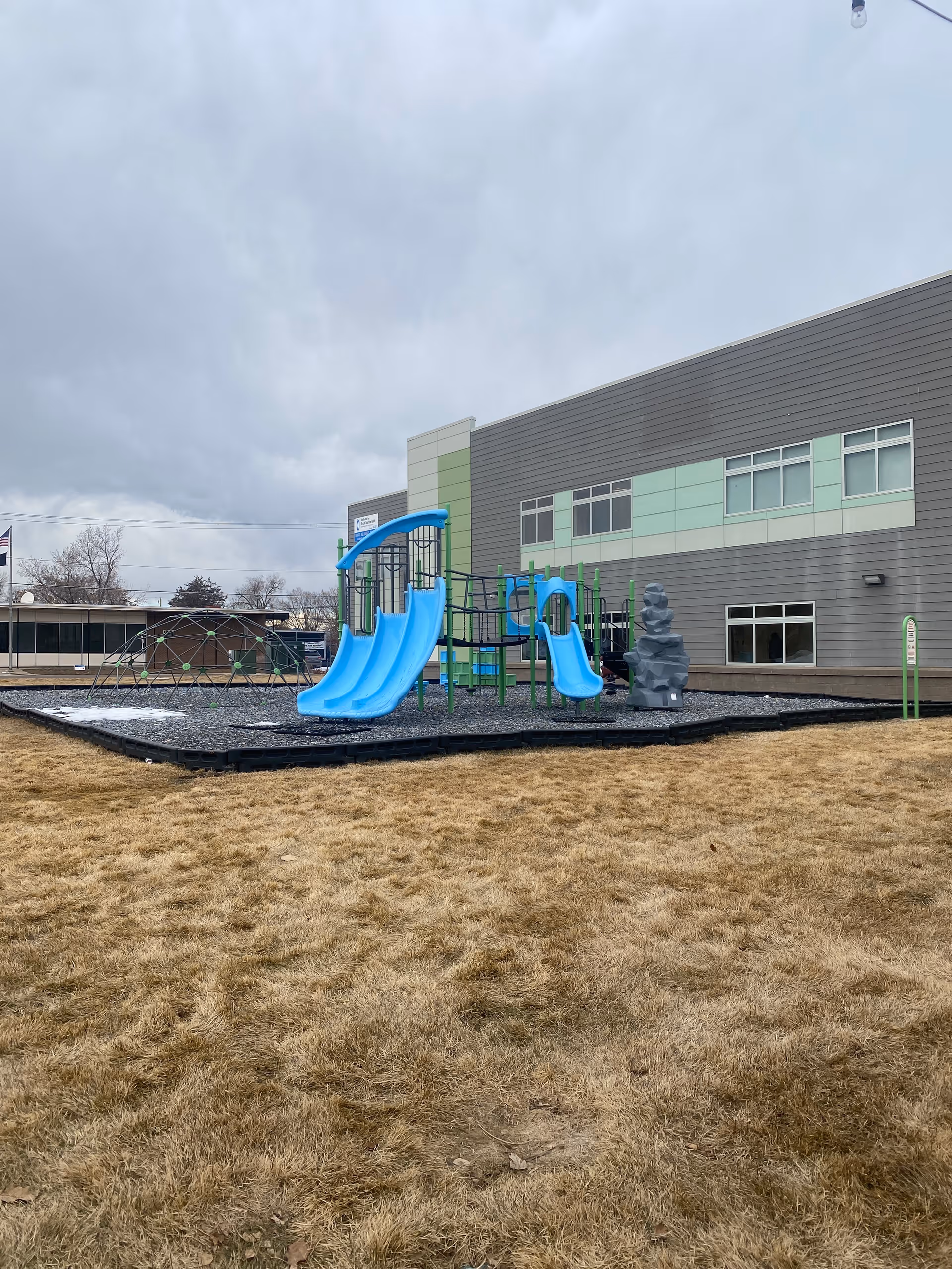 Outdoor playground with blue slides and climbing structure beside a modern facility building.