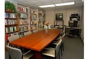A rectangular wooden conference table with chairs in a library-like room lined with bookshelves.