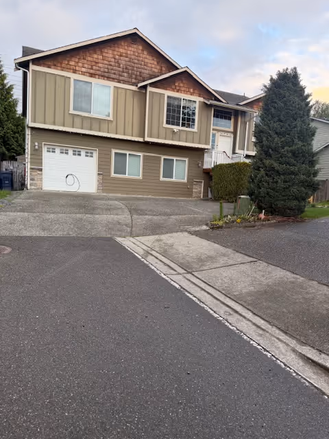 Two-story beige townhouse-style facility exterior with a garage, driveway, and street in foreground.