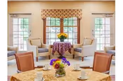 Bright communal lounge with round tables, chairs, and floral centerpieces by large windows.