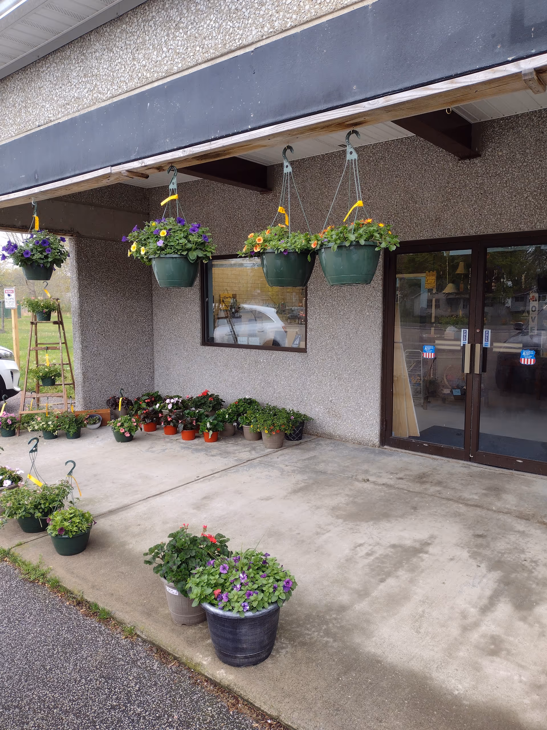 Exterior of a senior living facility entrance with hanging planters and potted flowers.