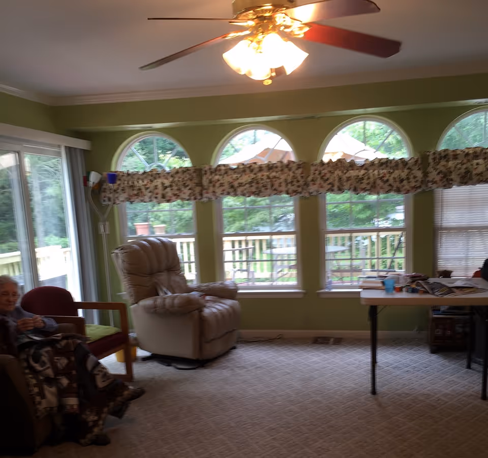 Bright green living room with arched windows, floral valance, recliner, table, and a resident.