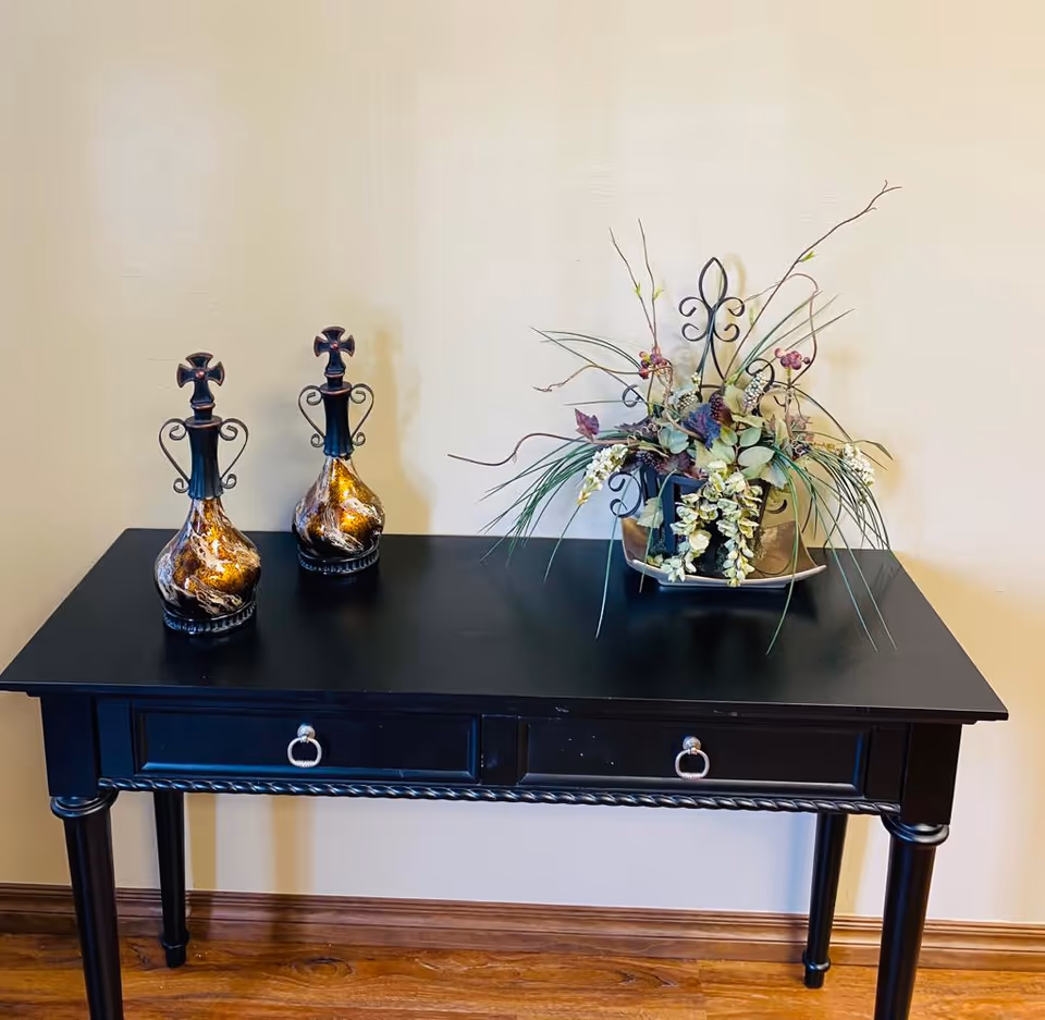 Black console table with two ornate decanters and a floral arrangement.