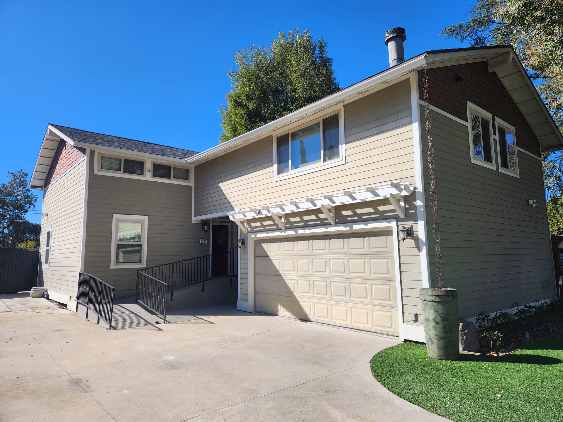 Two-story beige senior living facility with a double garage, entry stairs, and bright blue sky.