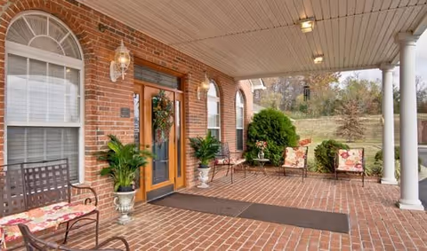 Covered brick front porch with seating, potted plants, and a double glass entry door decorated with a wreath.