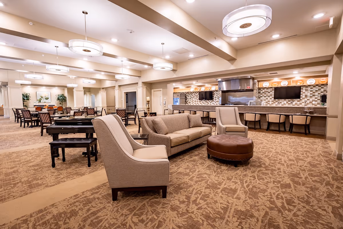 Spacious senior living lounge with seating, a bar area, and a pool table.