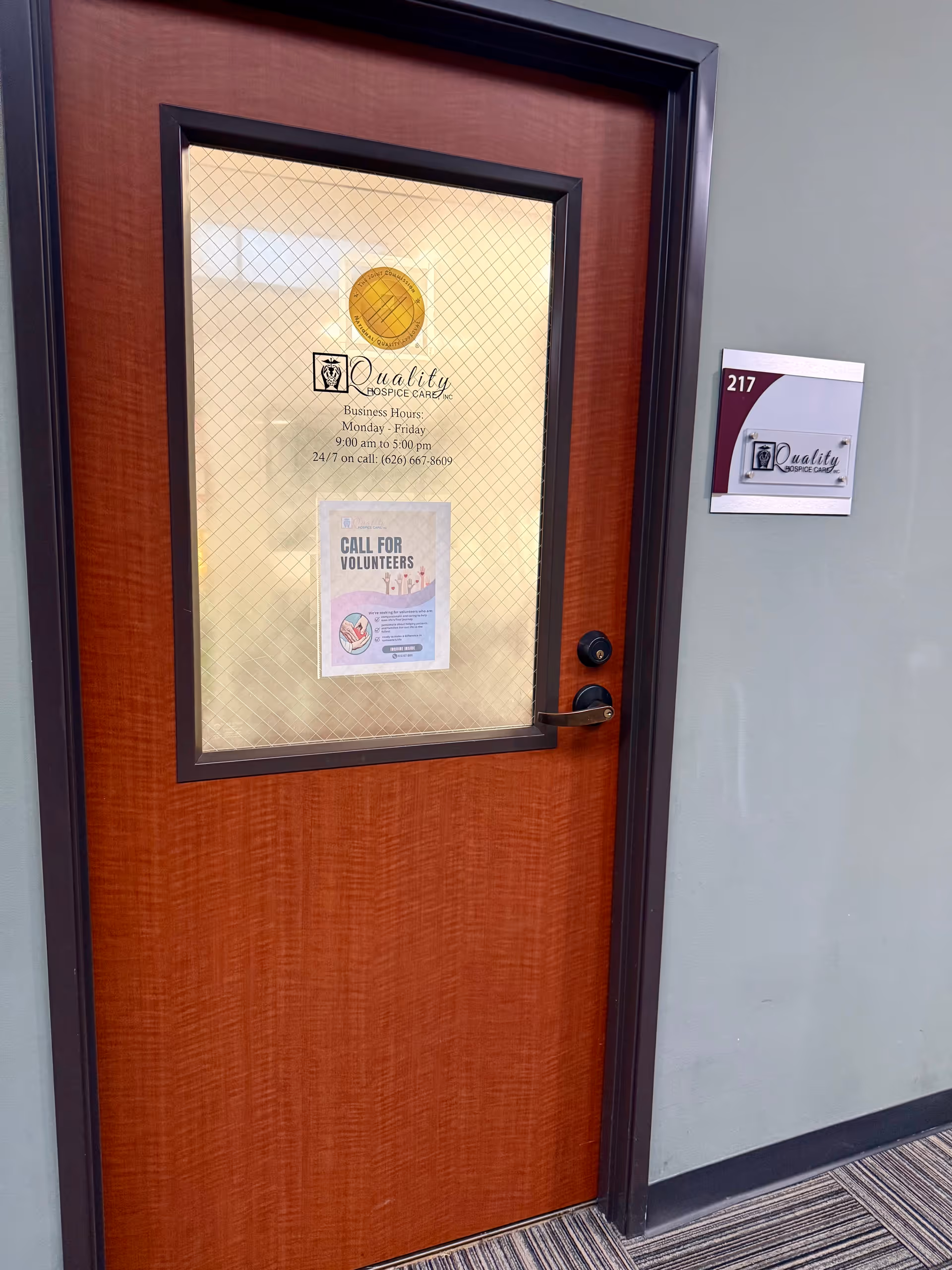 Orange door with frosted glass panel and Quality Hospice Care signage near room 217.