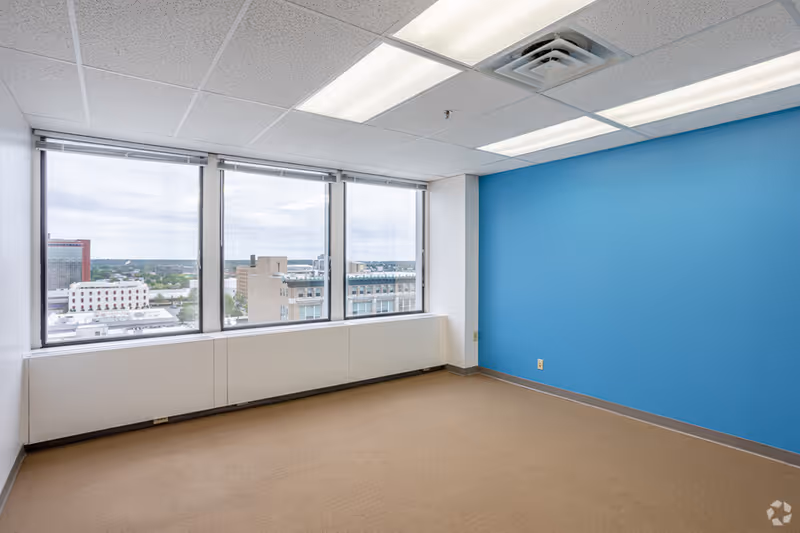 Bright empty room with a blue accent wall and large city-view windows.