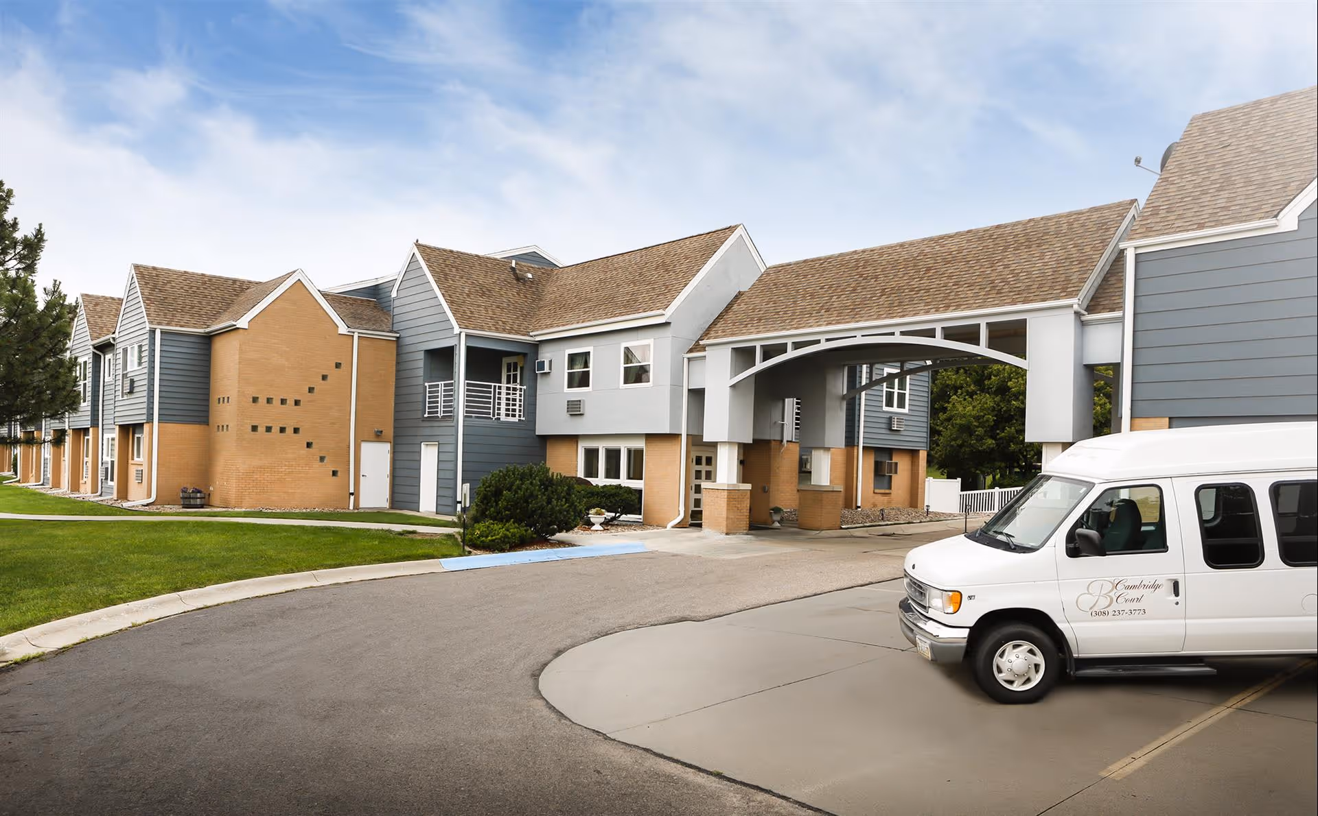 Exterior of Cambridge Court Apartments showing the building front with a covered porte-cochère and a white shuttle van parked in front.