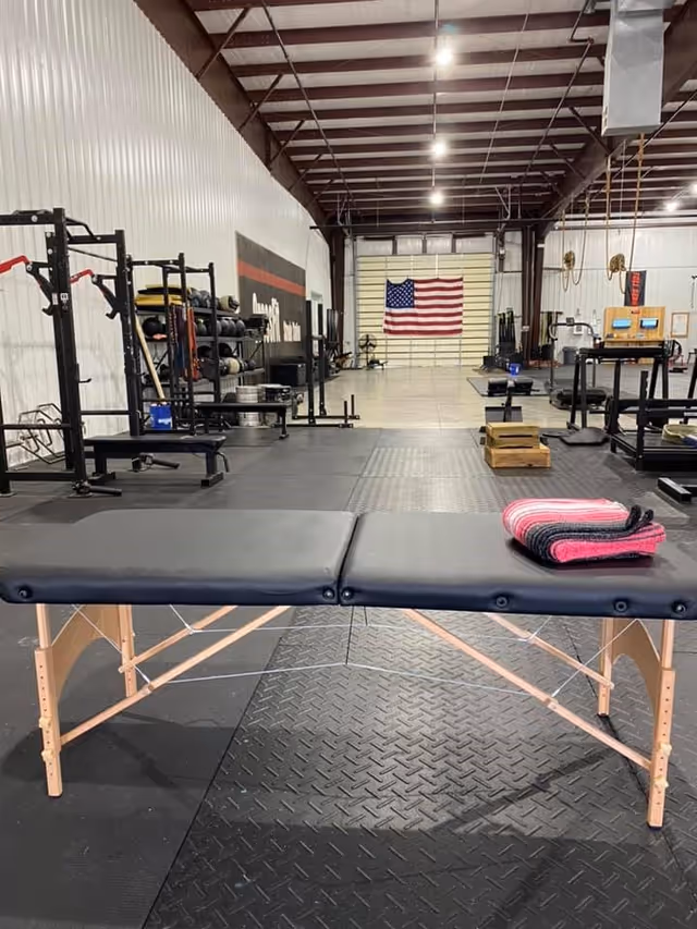 A PT gym interior with weight racks, mats, and an American flag.