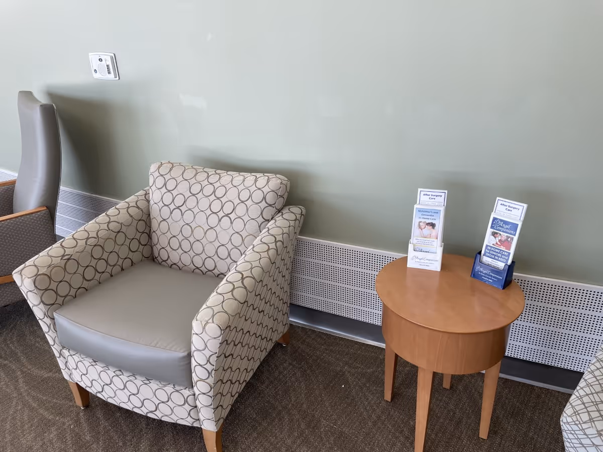 A patterned armchair beside a small round table with brochures in a quiet waiting area.