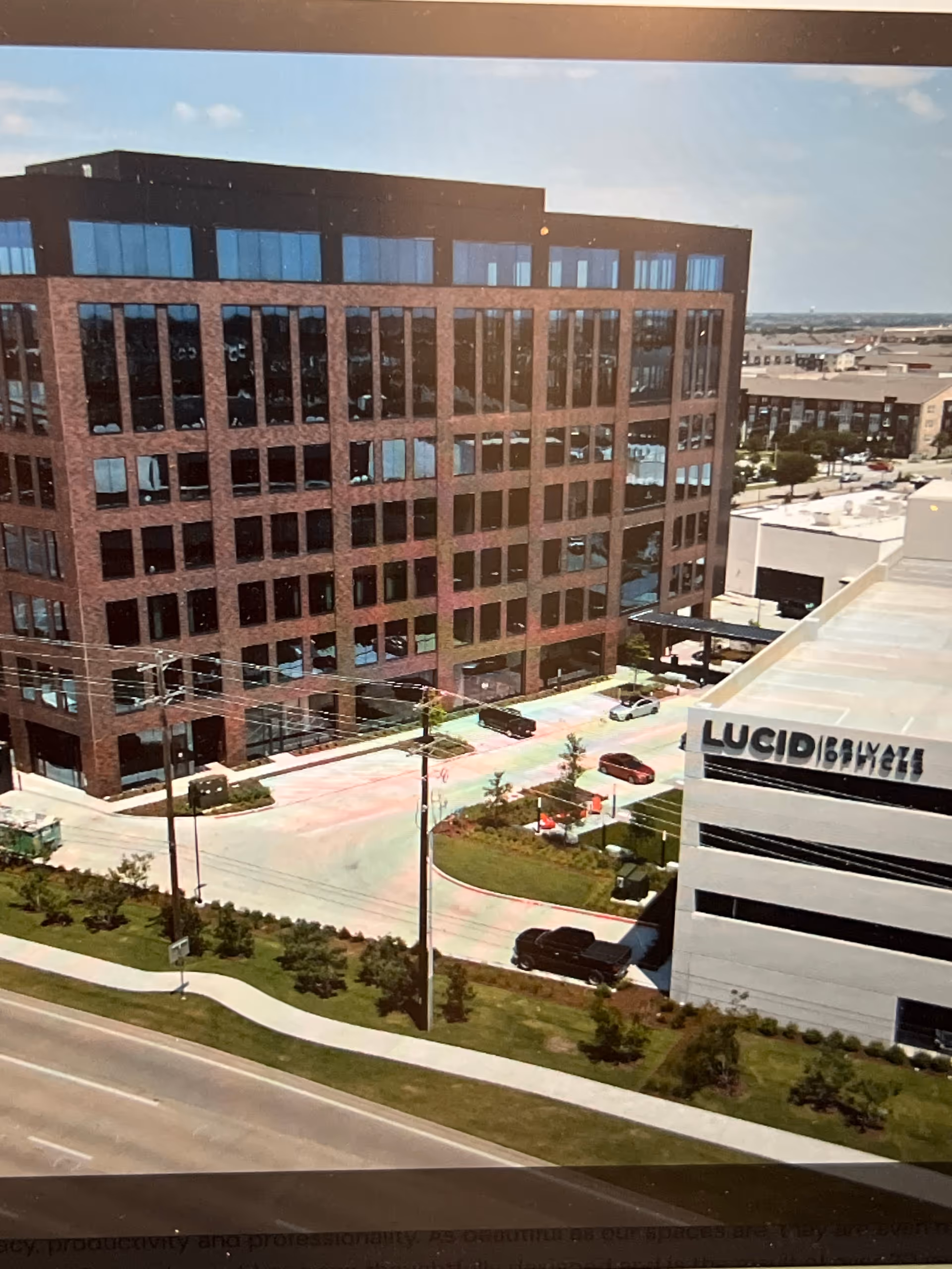 Exterior view of a tall brick office building beside a white building labeled Lucid.