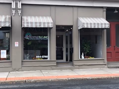 Street-front storefront of At Home TLC, Inc. with striped awnings and glass entry.