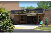 Brick building entrance with Bethel Estates sign, bench, and walkway.