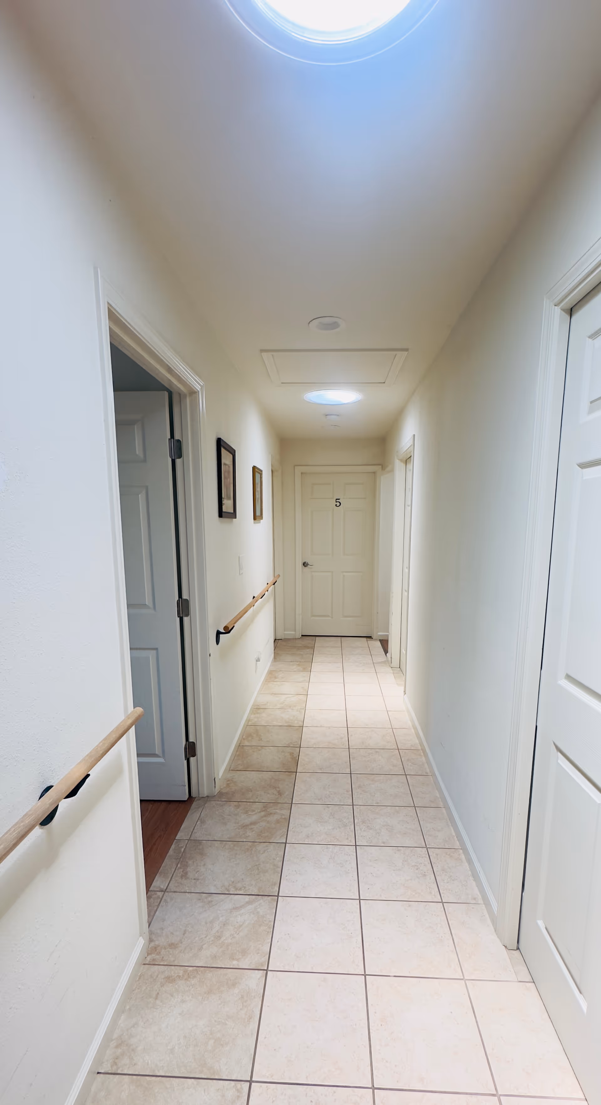 Long white hallway in a senior living facility with closed doors and tiled floor.