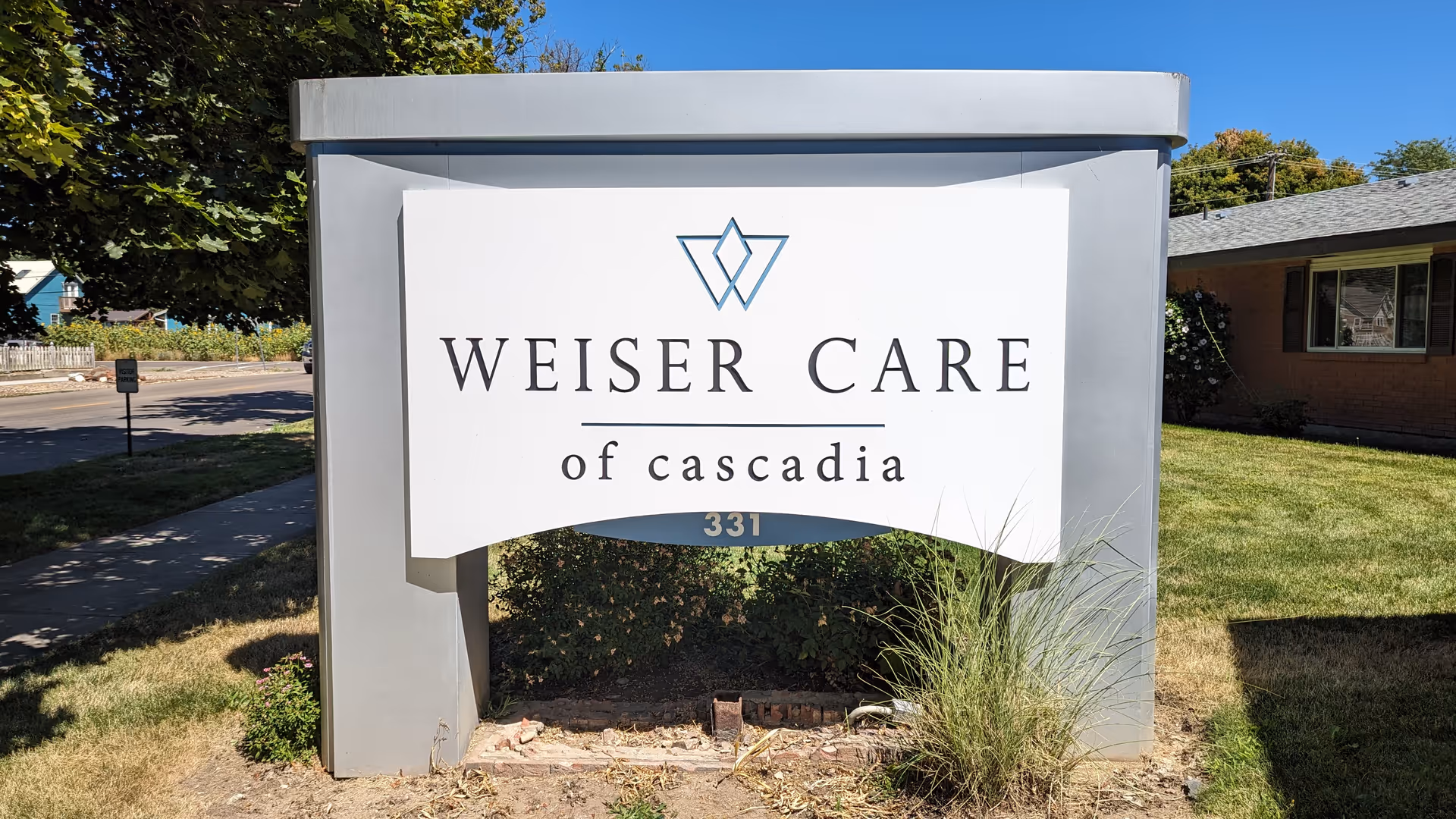 A large white sign reading Weiser Care of Cascadia beside a grassy entrance.