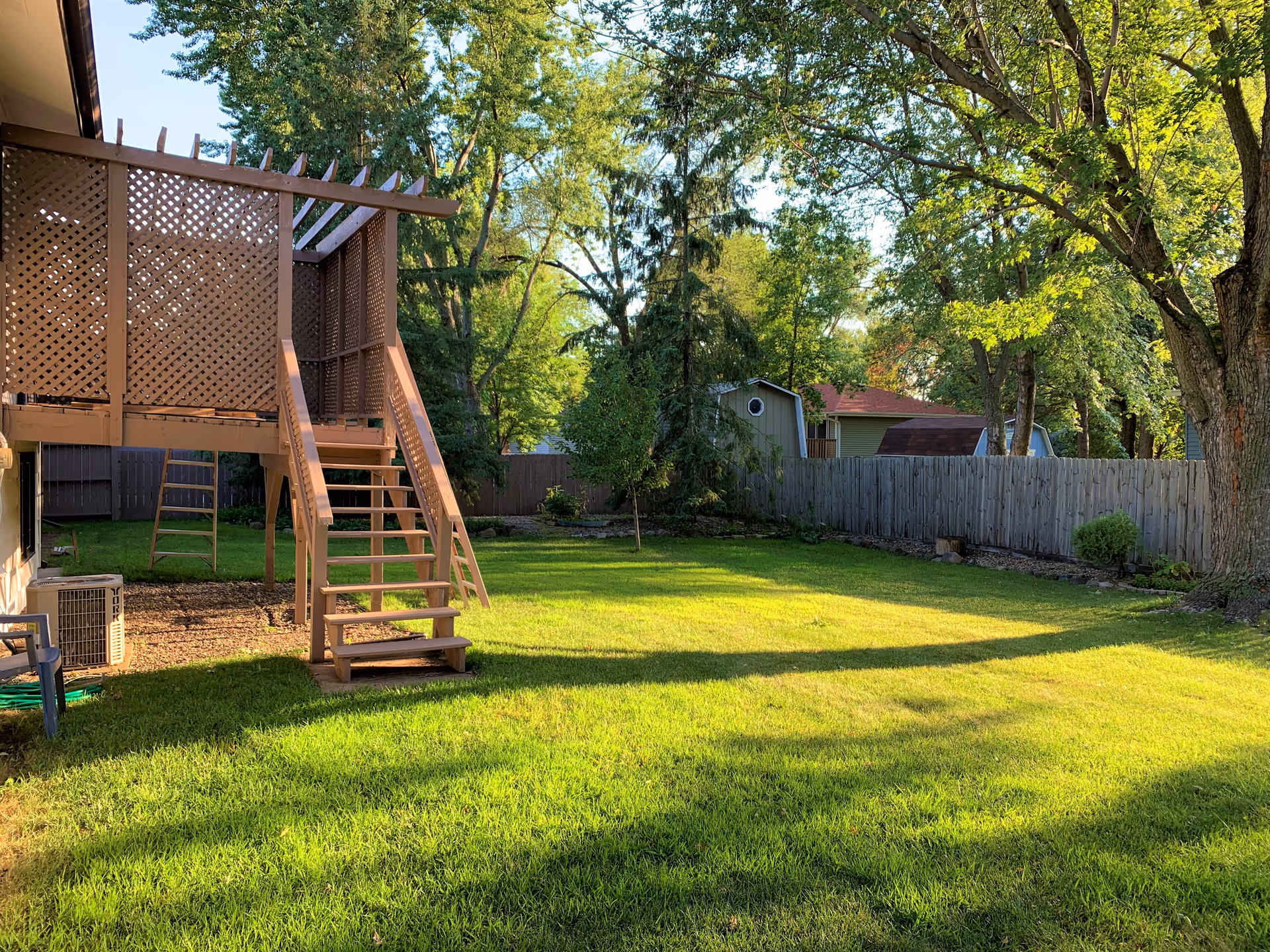 Backyard area with a raised wooden deck, stairs, fence, trees, and a shed.