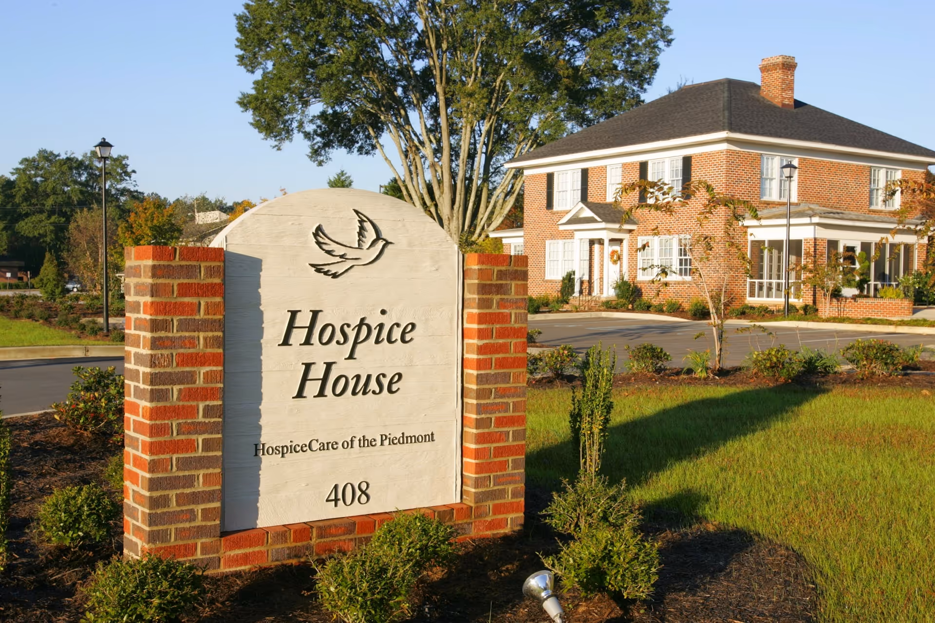 Brick hospice building with a sign reading Hospice House and manicured landscaping in front.