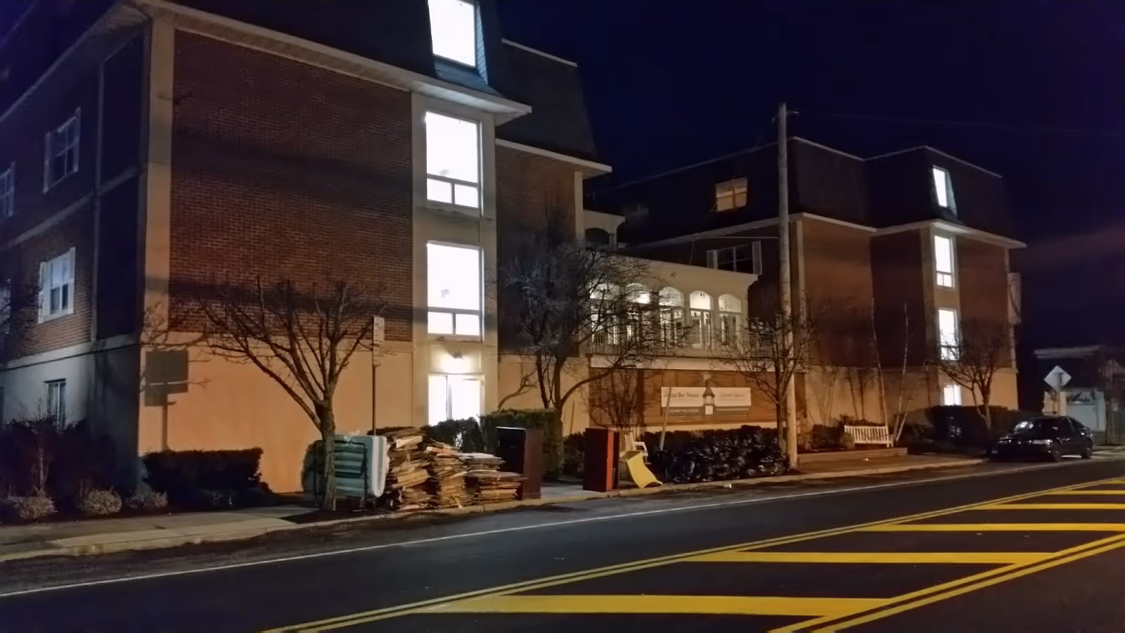 Nighttime exterior view of Harbor House Assisted Living building along a street with pallets nearby.