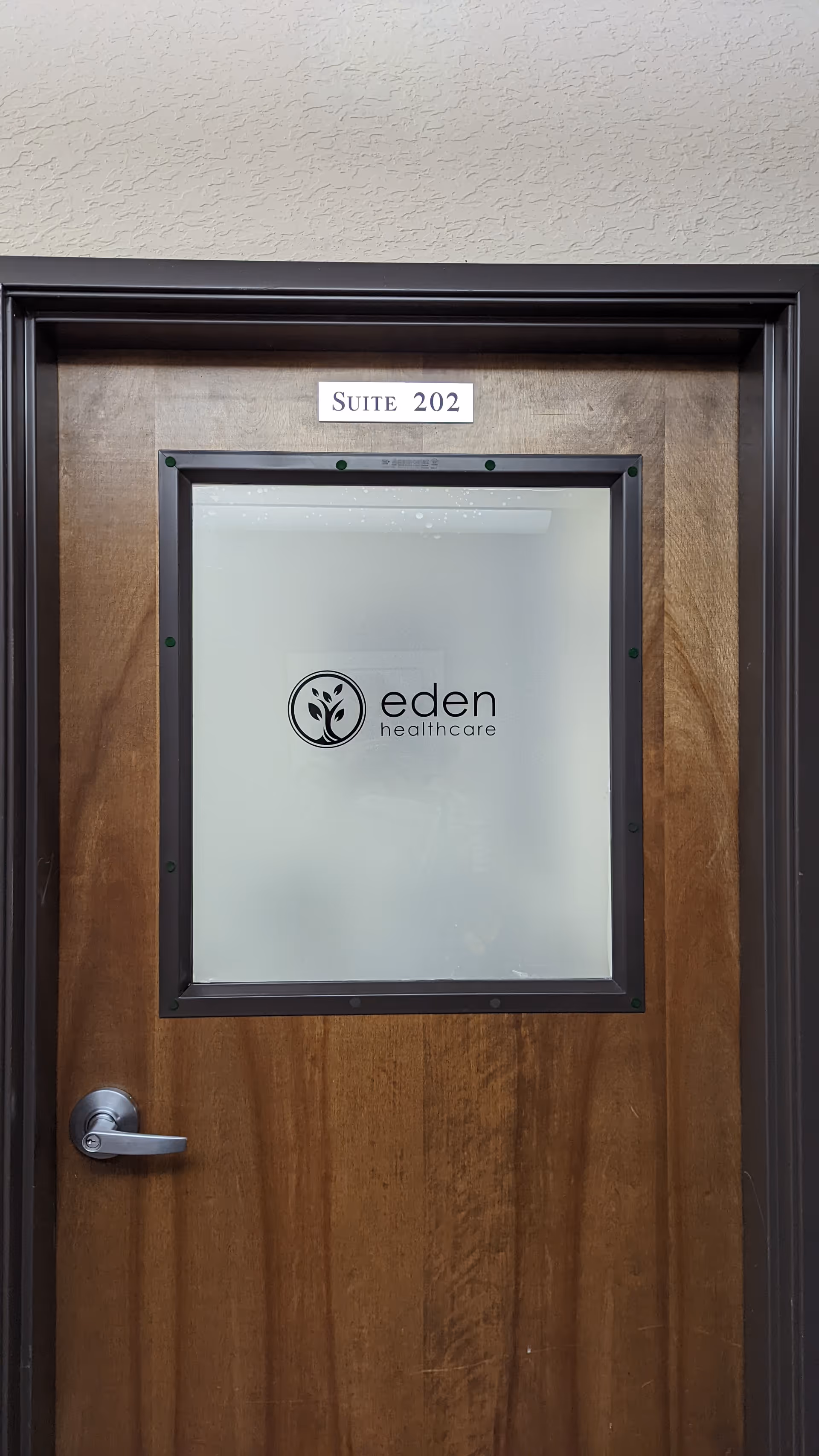 Wooden door with frosted glass window displaying Eden Healthcare logo and Suite 202 sign.