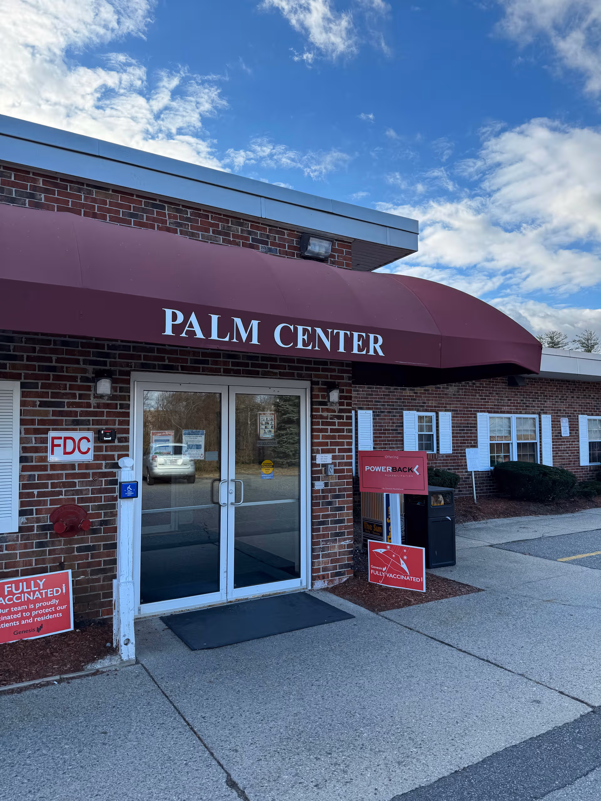 Brick facility exterior with a maroon Palm Center awning above glass entrance doors.