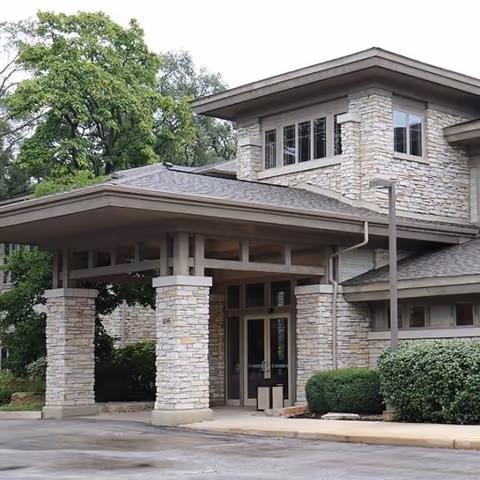 Exterior of a stone-clad senior care facility with a covered entrance and glass doors.