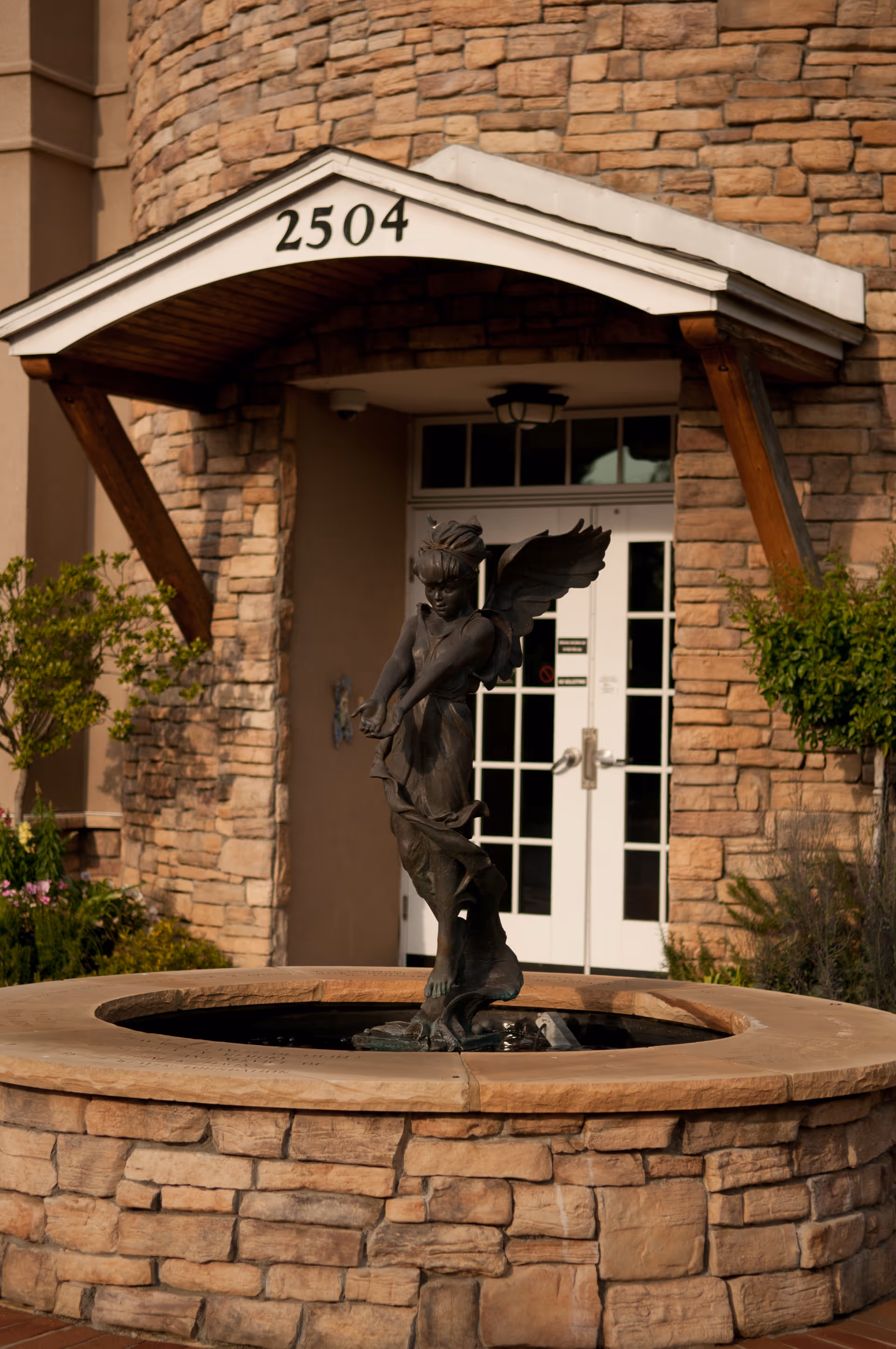 Stone exterior with an arched entrance, address 2504, and a fountain statue in front.