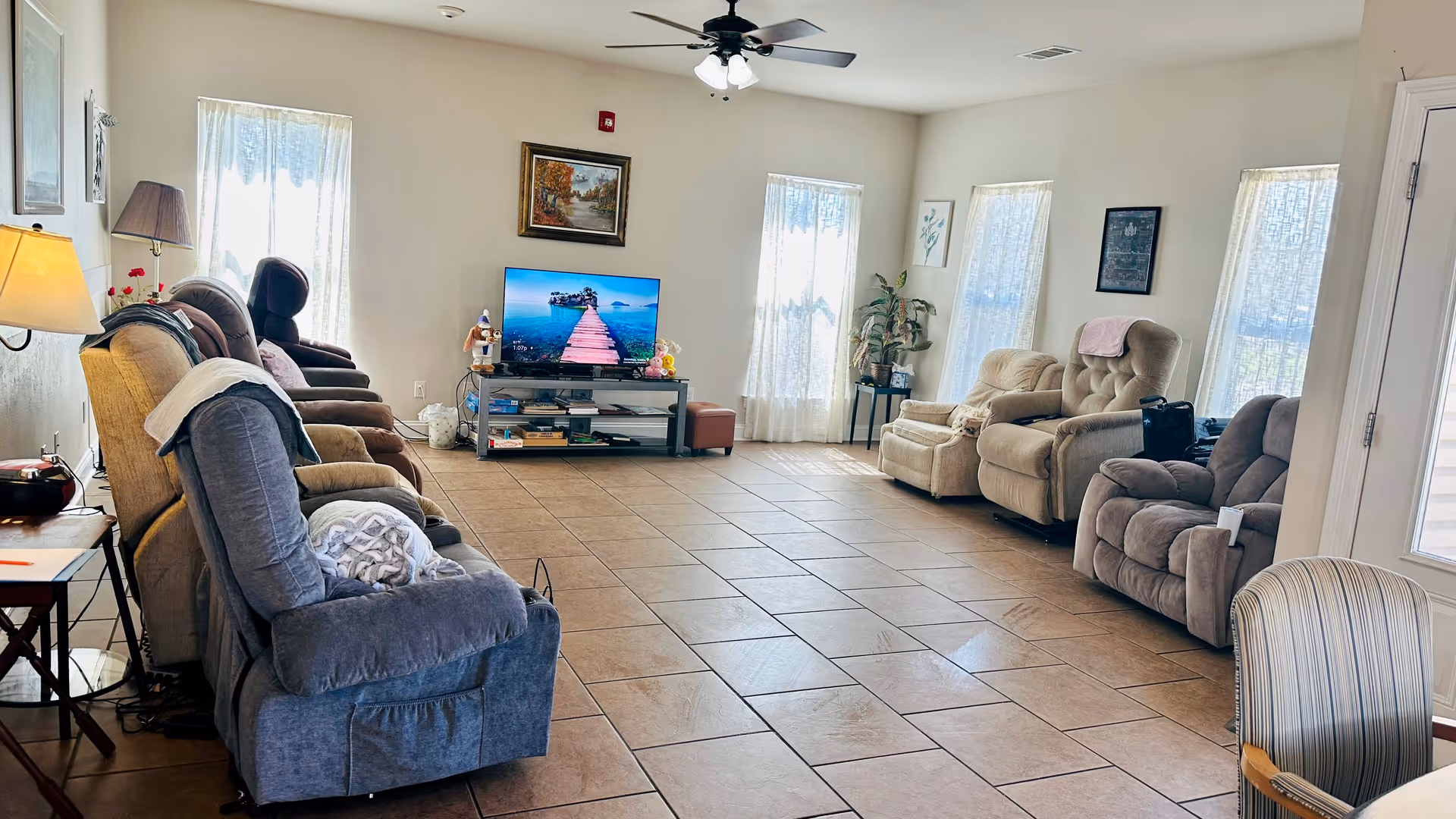 Spacious senior living lounge with recliners arranged around a TV and large windows.