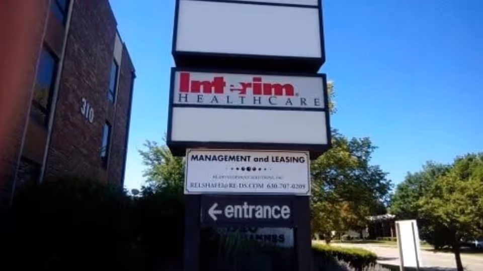 Outdoor sign for Interim HealthCare at the building entrance, with trees and parking area nearby.