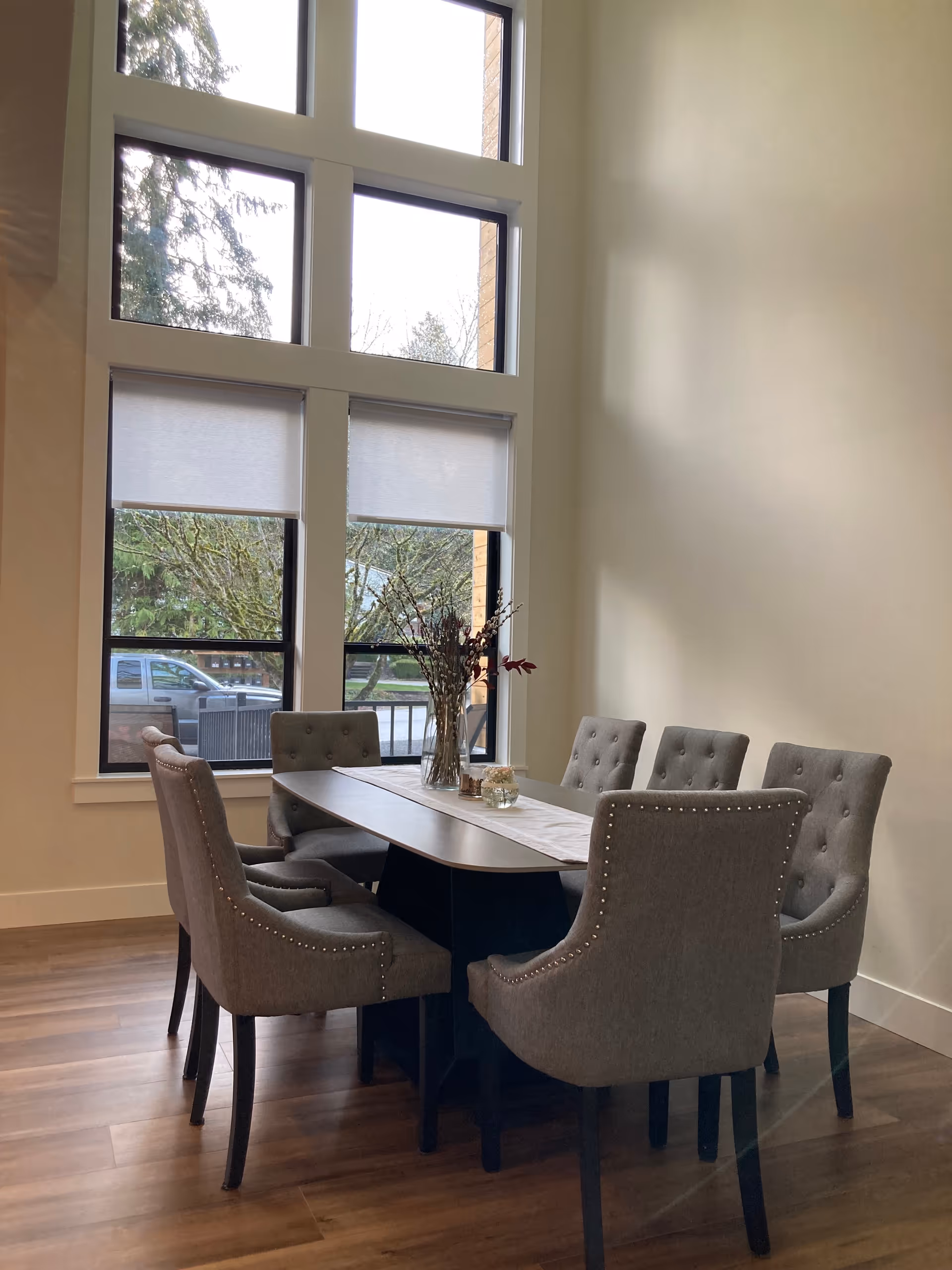 Six upholstered chairs surround a wooden dining table beside a large window.