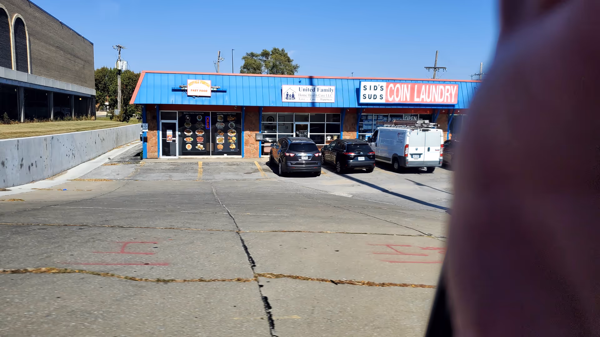 Exterior view of a strip mall storefront with a coin laundry sign and parked cars.
