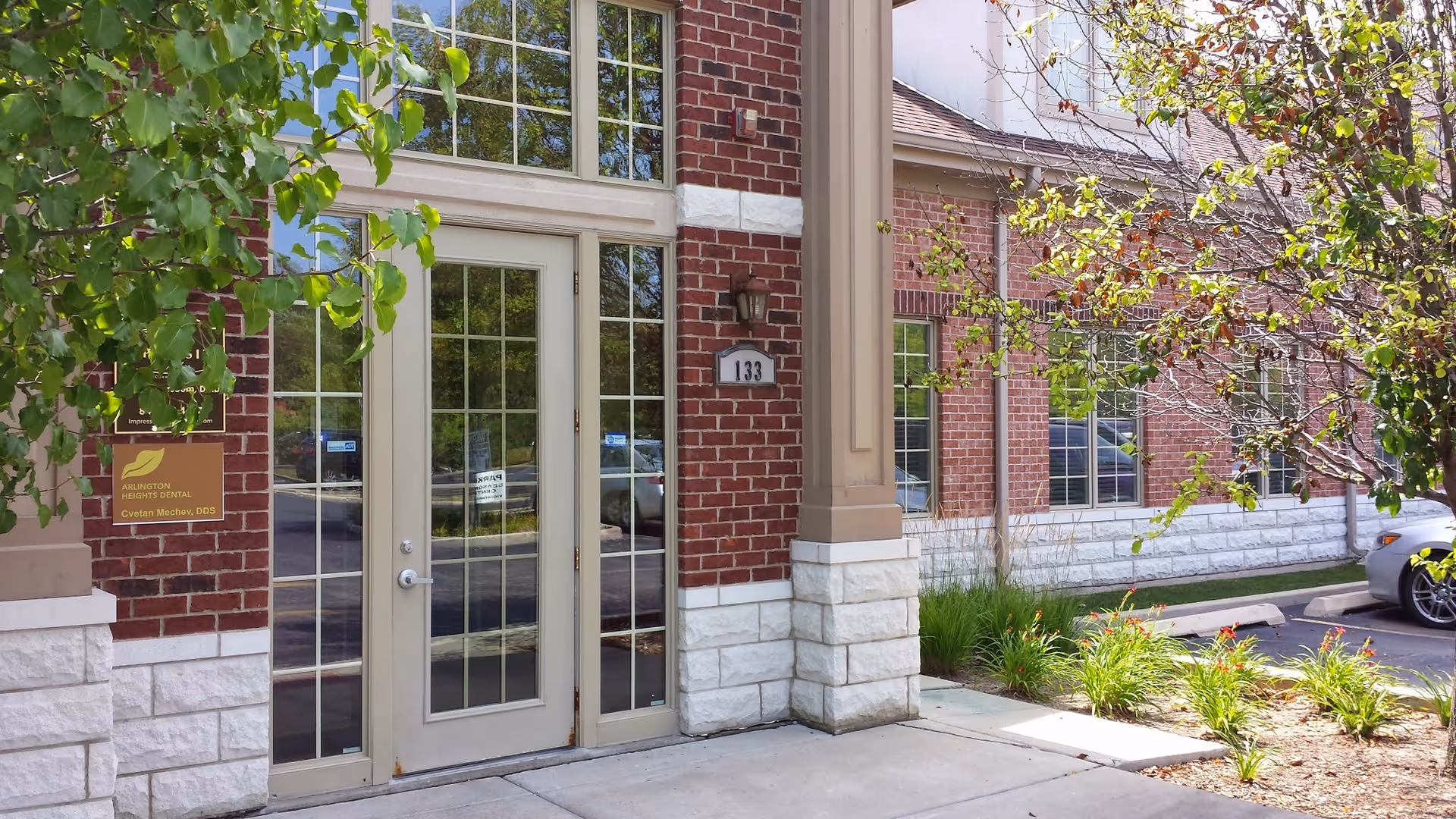 Brick senior living facility entrance with glass doors and landscaped walkway.