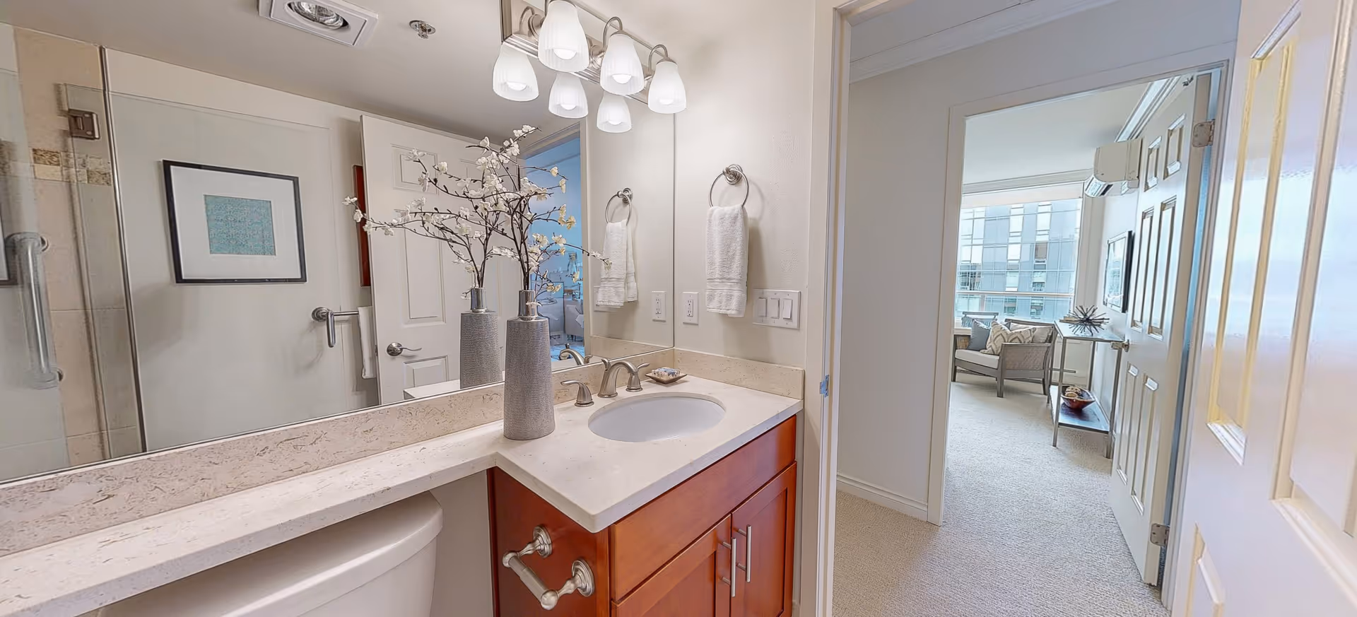 A bathroom vanity with sink, mirror, towel racks, and a view into a living area.