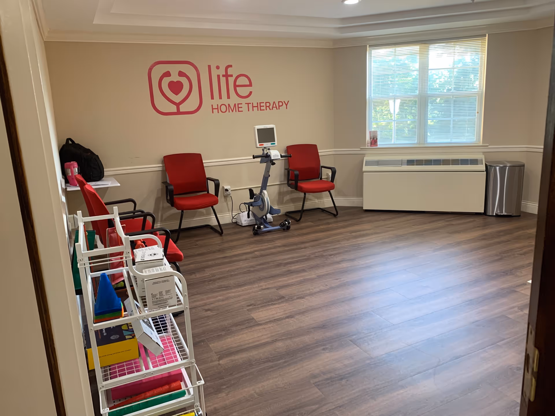 Therapy room with red chairs, exercise bike, and Life Home Therapy logo on wall.