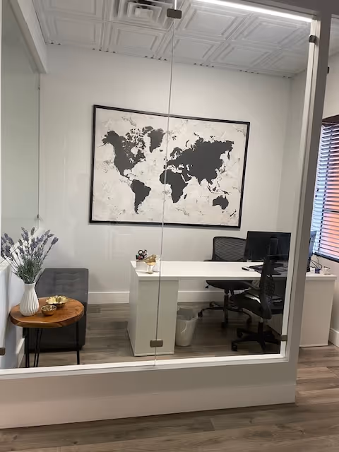 Glass-walled office inside a senior care facility, featuring a desk, world map art, and seating.