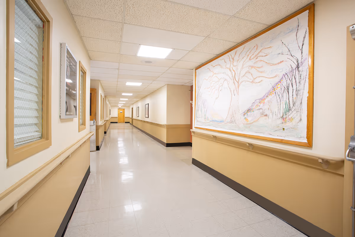 Long, well-lit hallway at Heritage Hall Clintwood with beige walls and framed artwork.