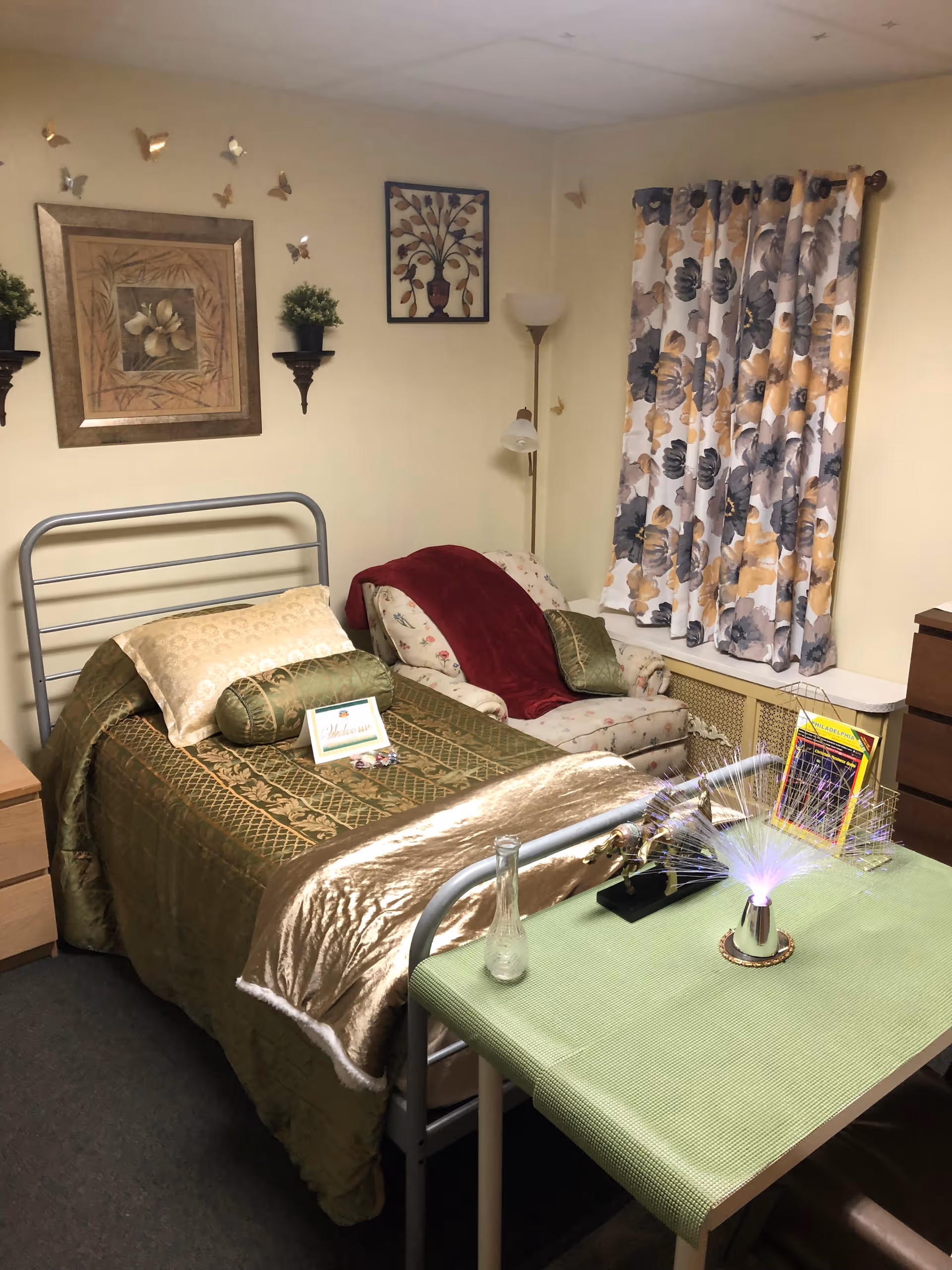 Cozy bedroom with a metal bed frame, patterned bedding, floral curtains, and wall art.