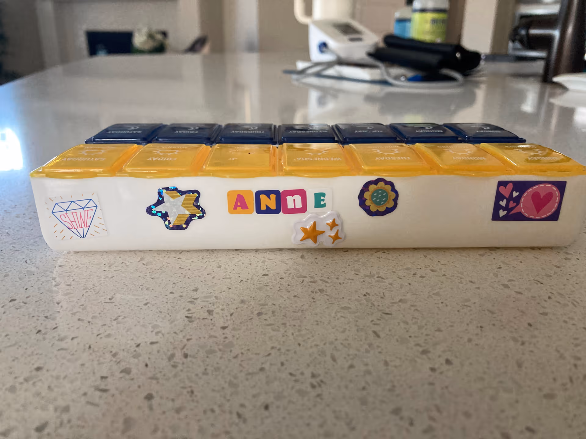 A colorful weekly pill organizer rests on a speckled kitchen counter.