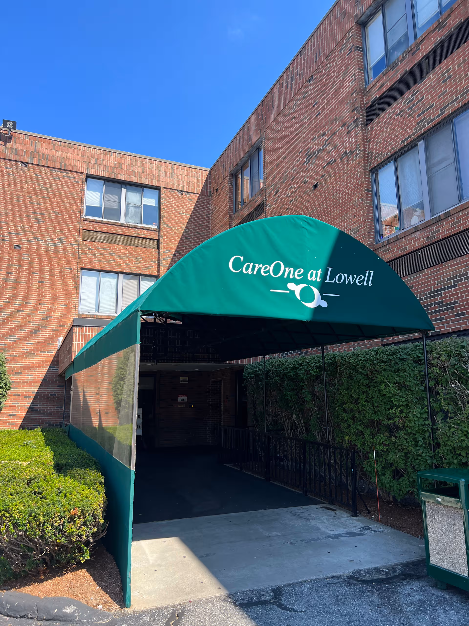 Brick senior living facility entrance with a green CareOne at Lowell canopy.