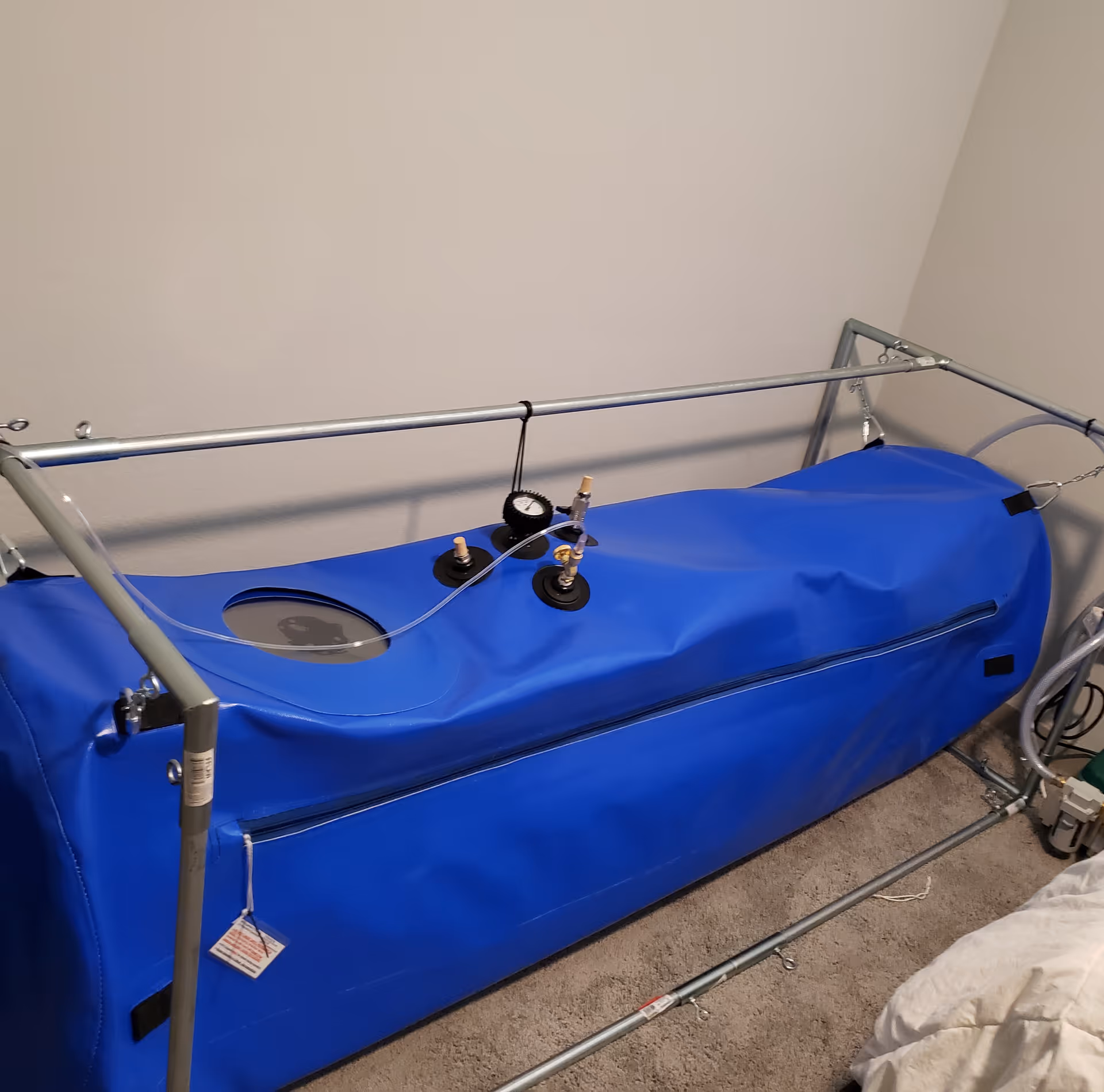 Blue hyperbaric therapy chamber inside a small light-colored room with metal frame