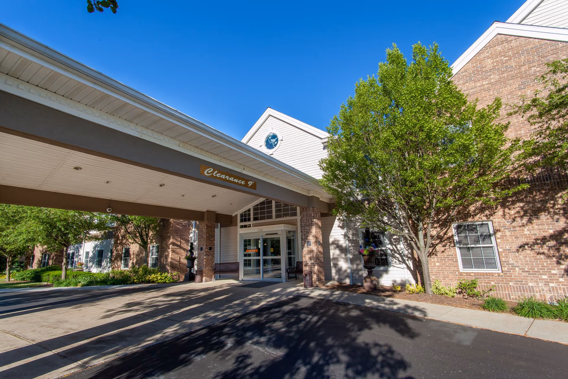 Exterior view of a brick retirement community entrance with a covered drop-off area and trees.