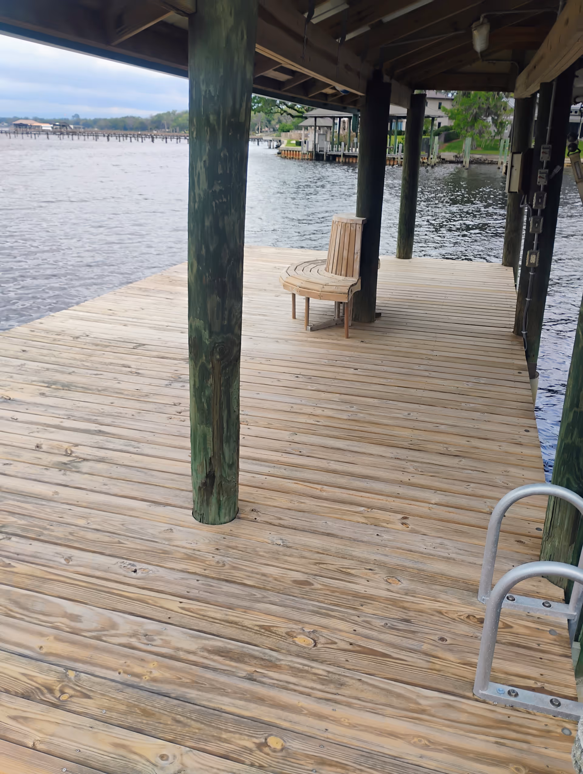 Wooden dock extending over water with green posts and a single chair.