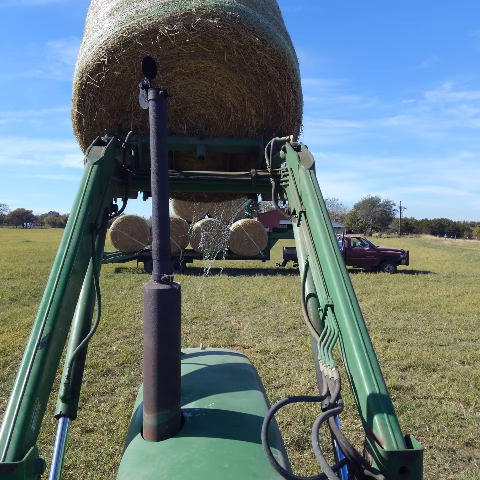 View from tractor front showing large round hay bale, field, and clear blue sky.