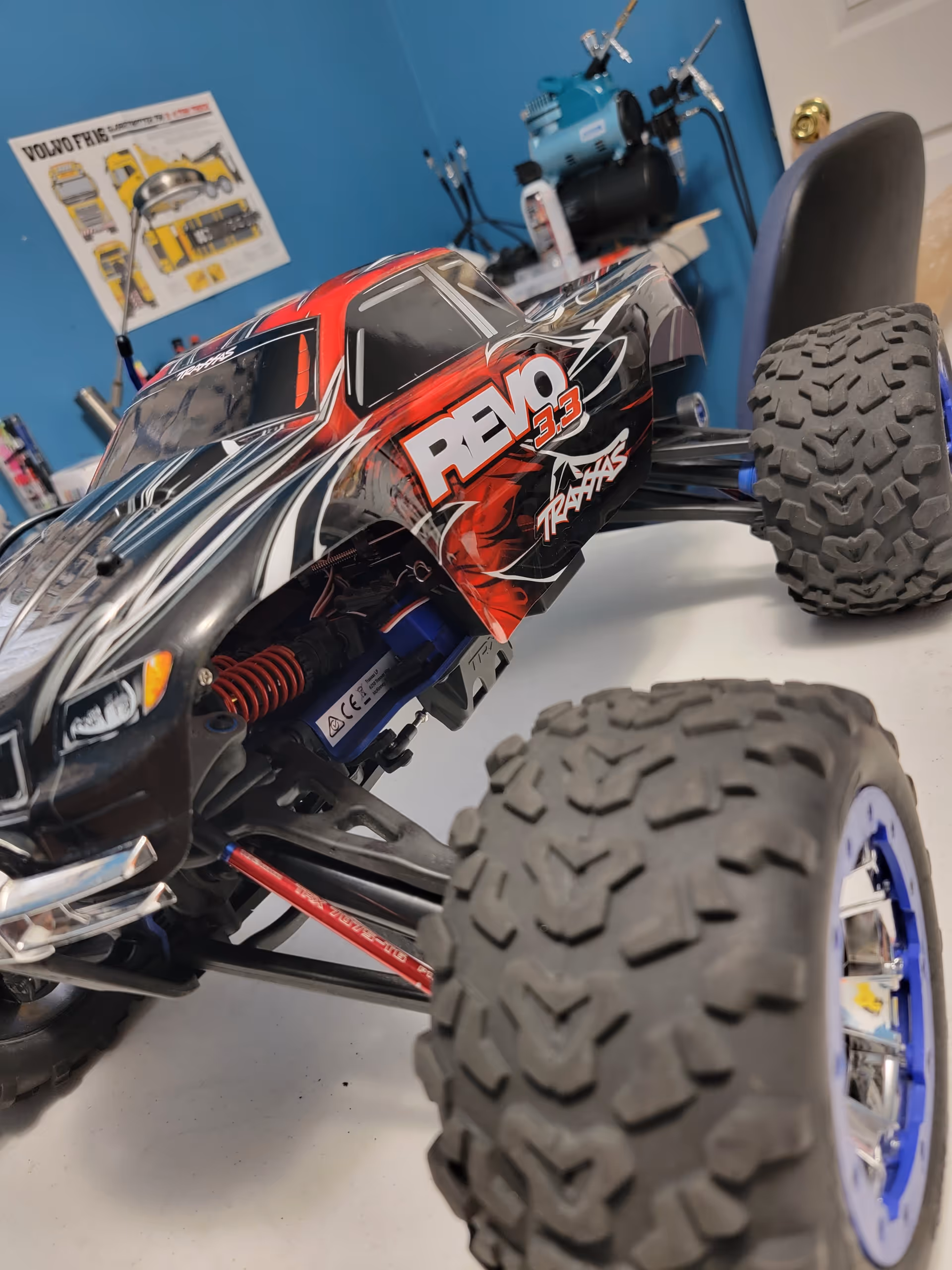 An RC off-road car sits on a workshop table with tools in the background.