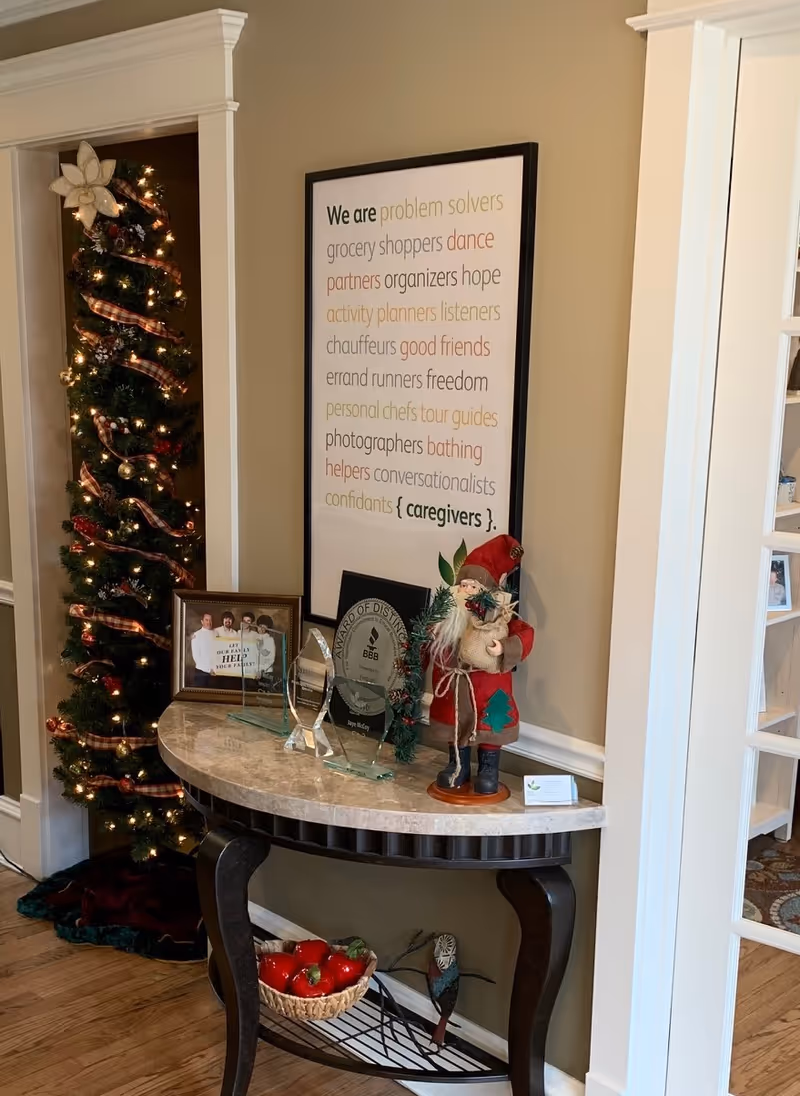 Festive foyer with Christmas tree, framed quote, awards on marble console table, Santa figure.