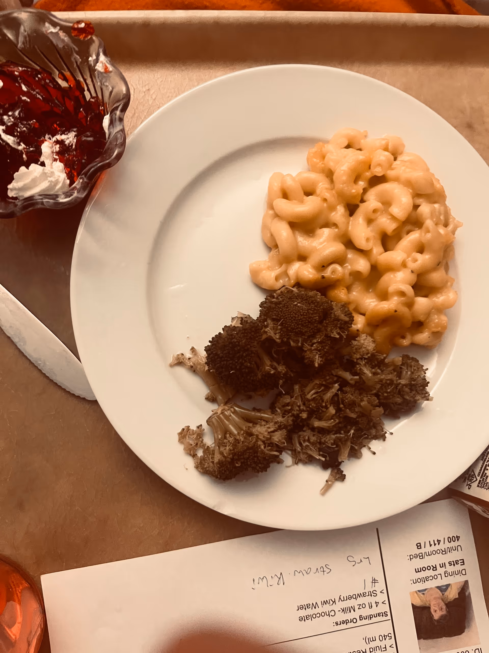 White plate with macaroni and cheese and broccoli on a dining table.