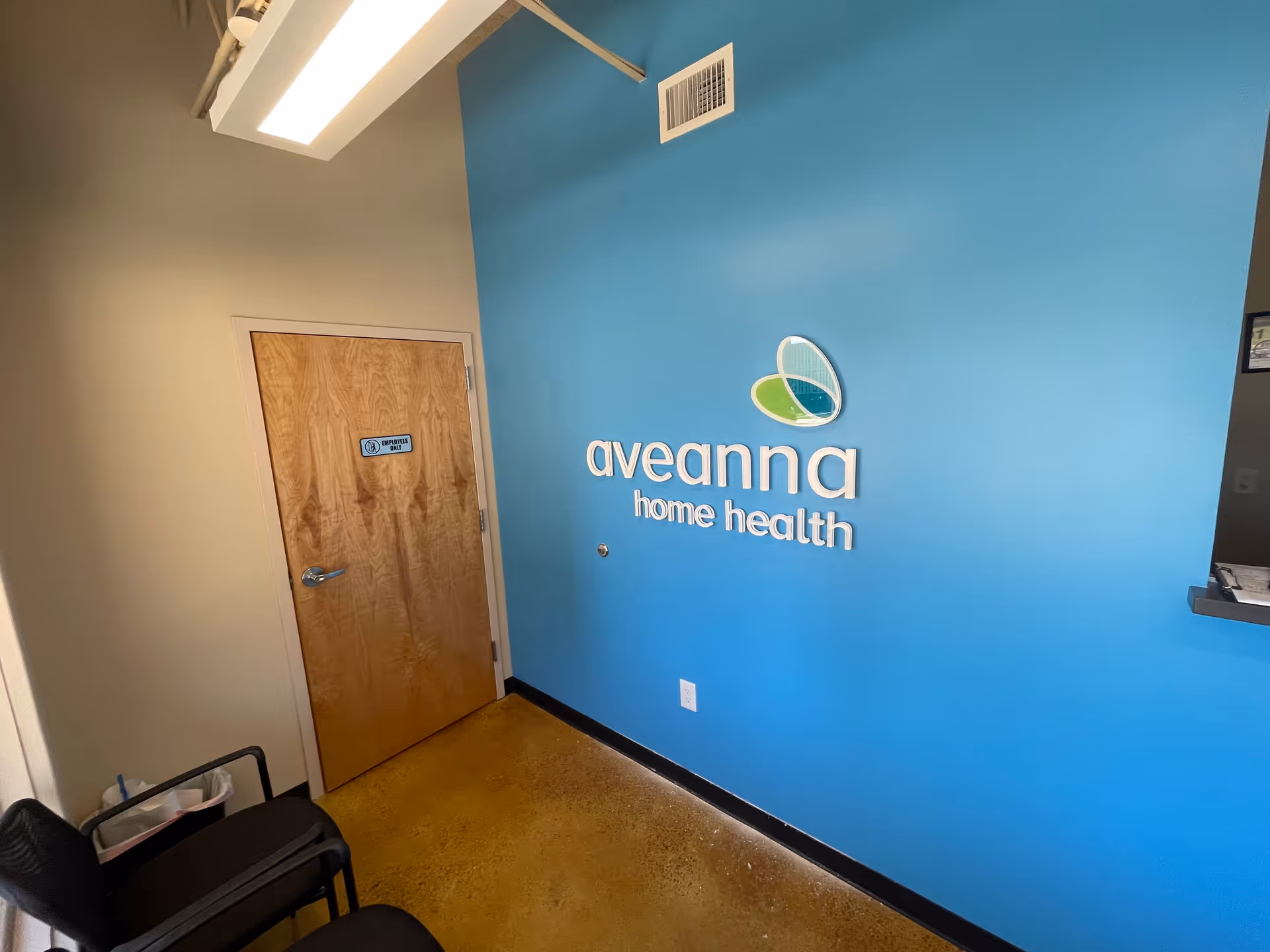 Blue wall with Aveanna Home Health logo beside a wooden door in a hallway.