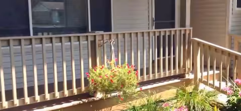 Exterior porch of a senior facility with wooden railing and flowering planters.