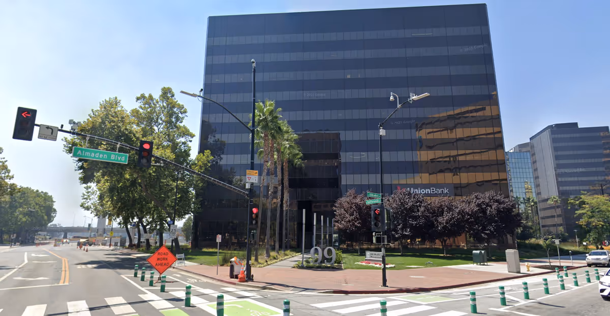 Tall modern glass-front office building along a busy city street with palm trees.